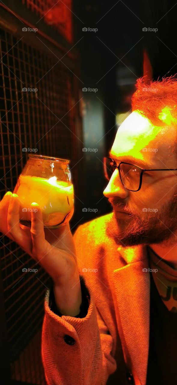 Man with candle and glasses in a bar under orange lights