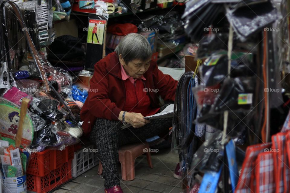 An Old Woman reading newspaper inside her store