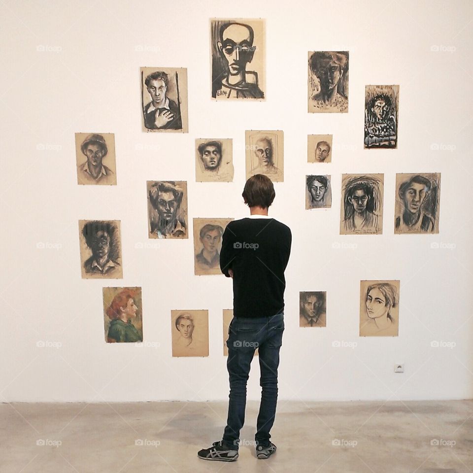 Young man looking at paintings on wall in art gallery