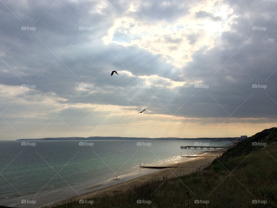 Sun bursting through the clouds at Bournemouth beach with birds flying in the foreground. Creating a god like scene. Sun beams. Angelic. Godly clouds. Heart in the sky. Heart in the clouds. Cloud heart 