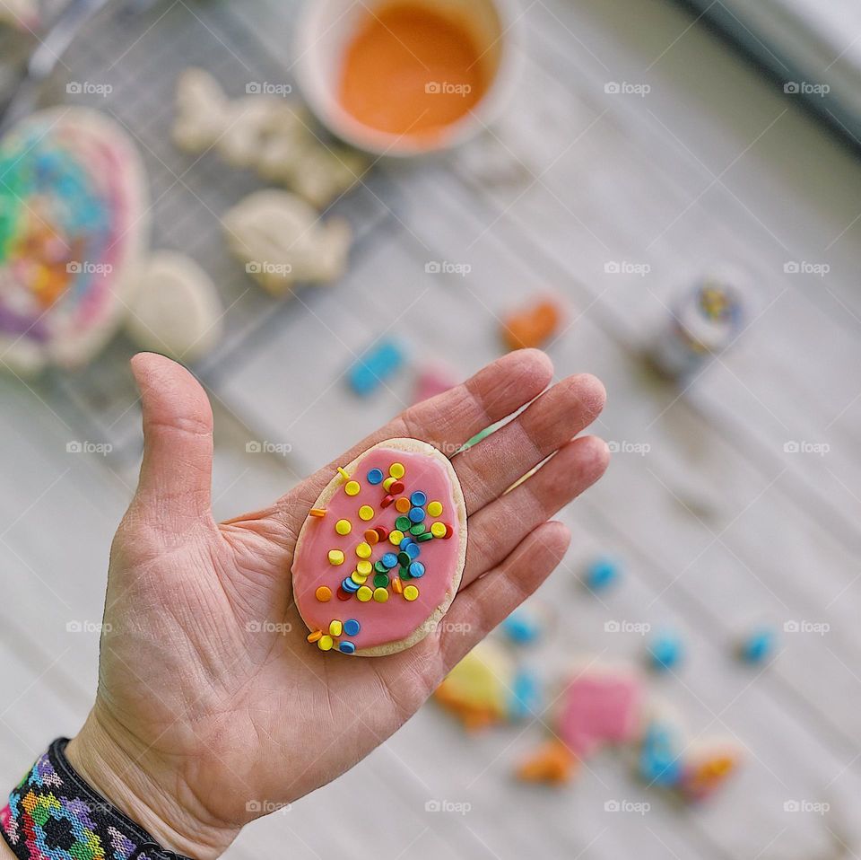 Woman’s hand holding Easter egg sugar cookie, making sugar cookies for Easter, first person point of view, hand holding cookie, proud of homemade sugar cookies, delicious sugar cookies covered in sprinkles 