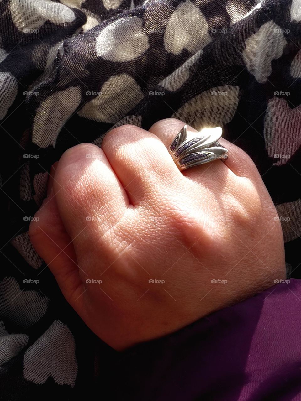 Hand wearing a flower-shaped ring with violet stones lying on a scarf and reflecting sunlight.