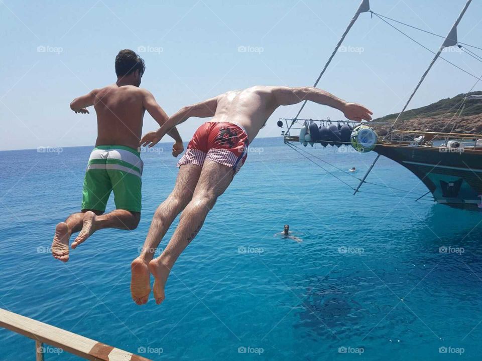 guys jumping off sailing boat onto blue sea