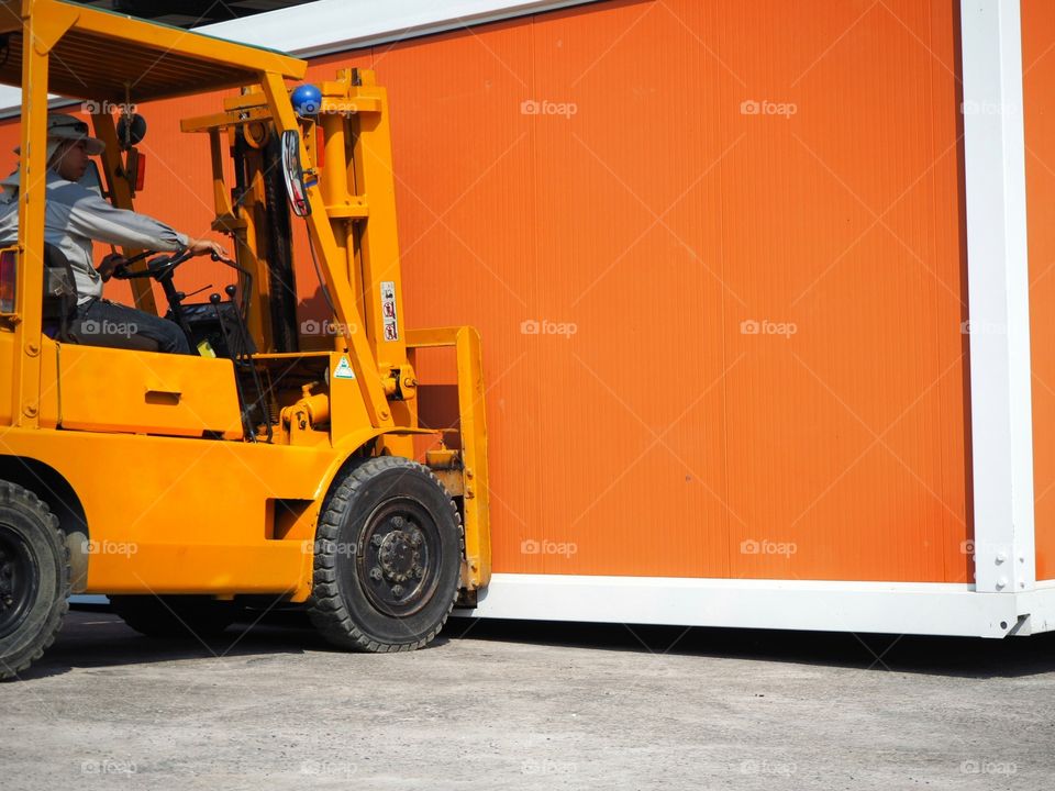 Forklift driver maneuvering while lifting an orange container.