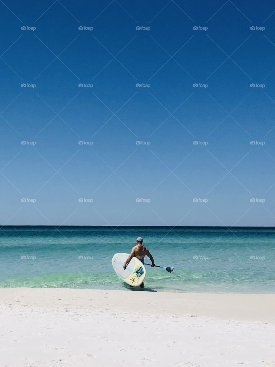 Man carrying paddle board into after at sunny beach 