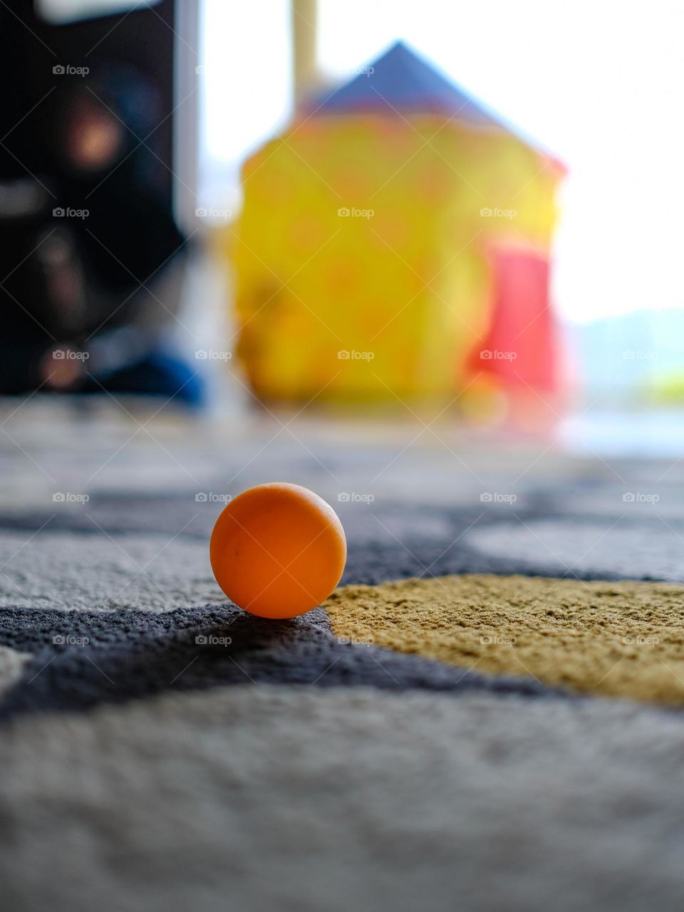 An orange pingpong ball on the carpet with children tent in the background