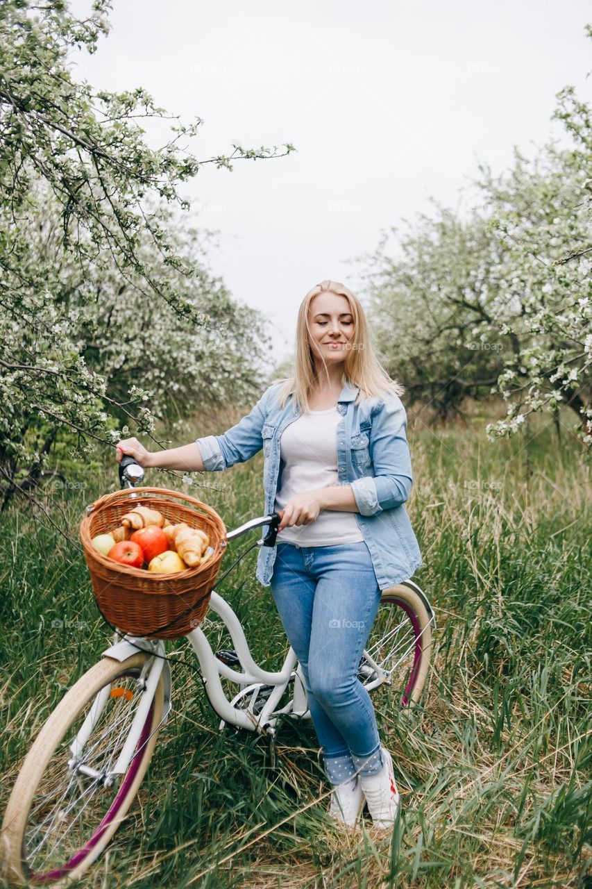 Happy blonde girl in jeans clothes holding bicycle and close eyes