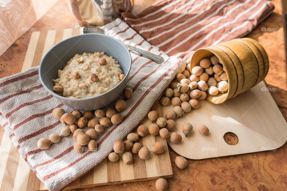 Cooked oatmeal in a deep gray plate with hazelnuts and honey.