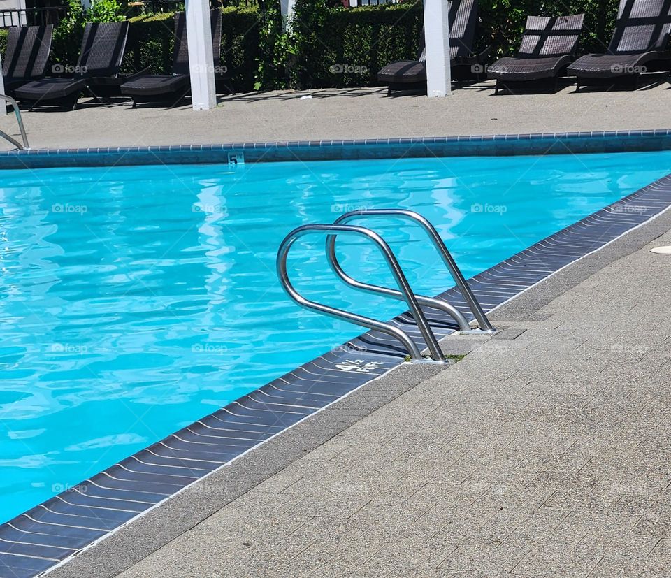 poolside lounge chairs overlooking shimmering clear bright blue water on Sunny Summer day in Oregon suburbs