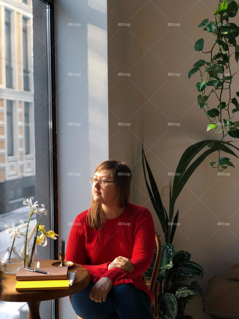 A woman in a red sweater sits by the window 