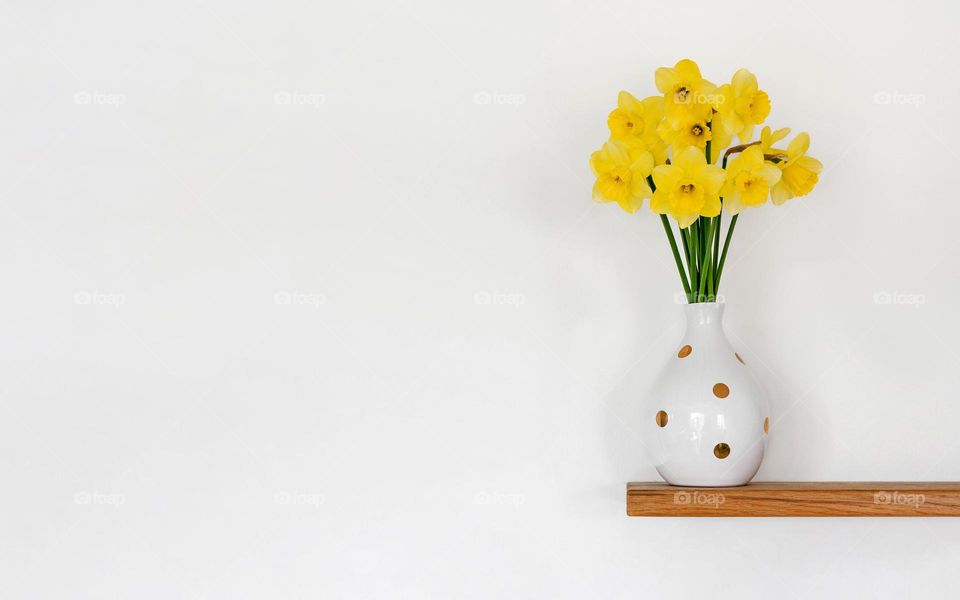 Minimalist photo of beautiful yellow daffodils in vase on floating shelf