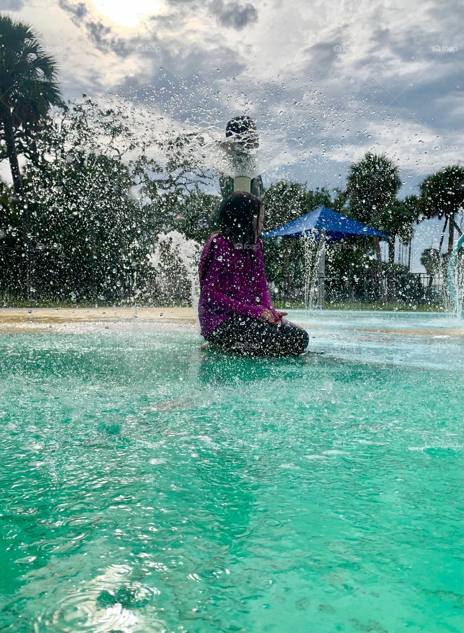 Children having lots of fun in the water at the colorful kids splash pad at the city park for children during a really warm day in Florida.