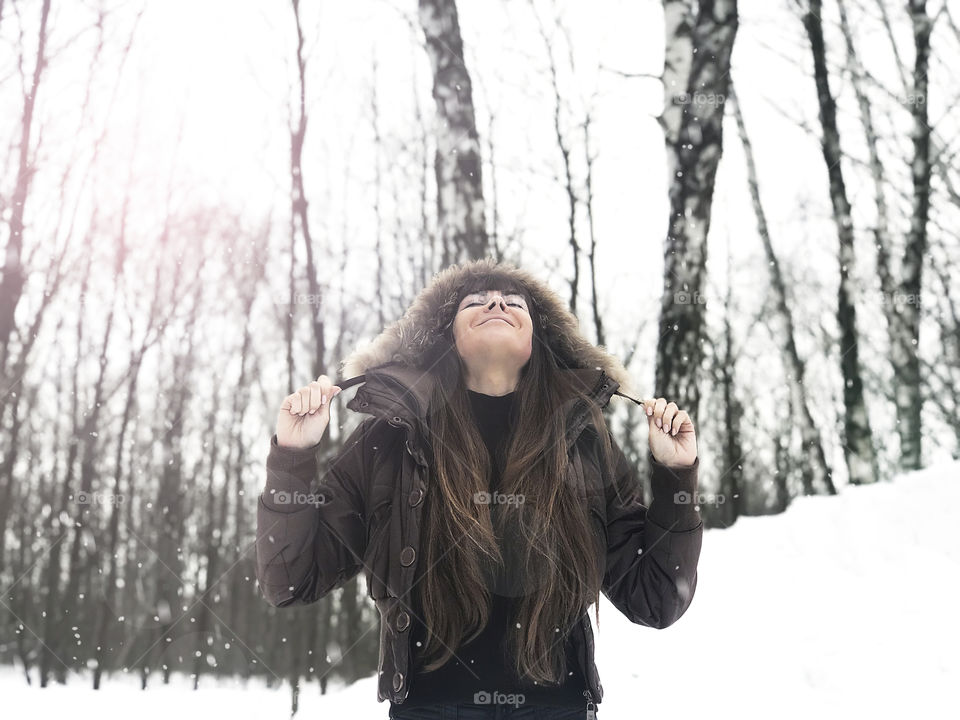 Young woman enjoying falling snow in forest 