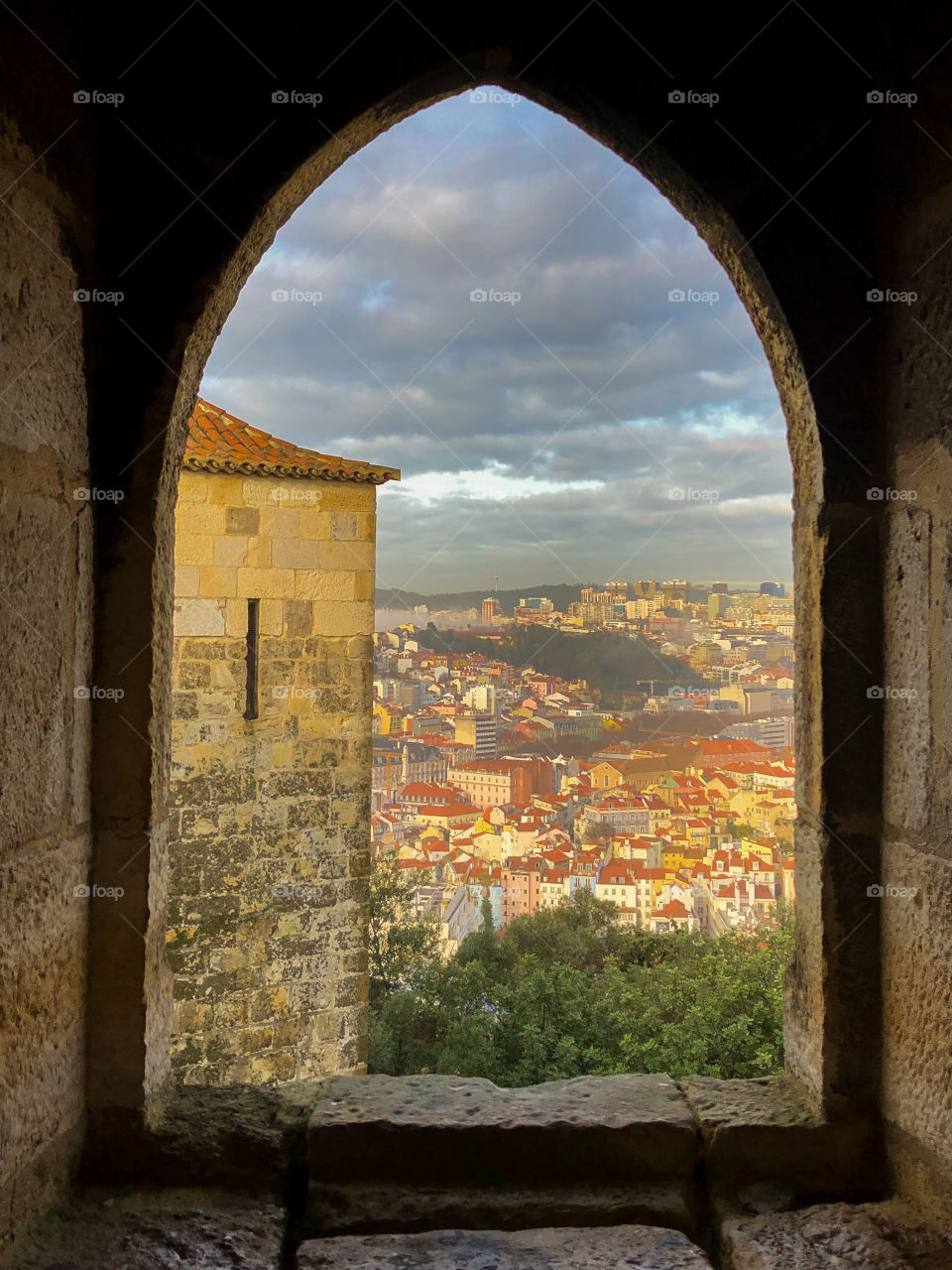 The city of Lisbon is perfectly framed within a window of a castle tower atop a hill