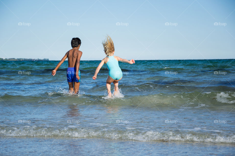 Young children jumping in the water at Höllviken beach in Sweden.