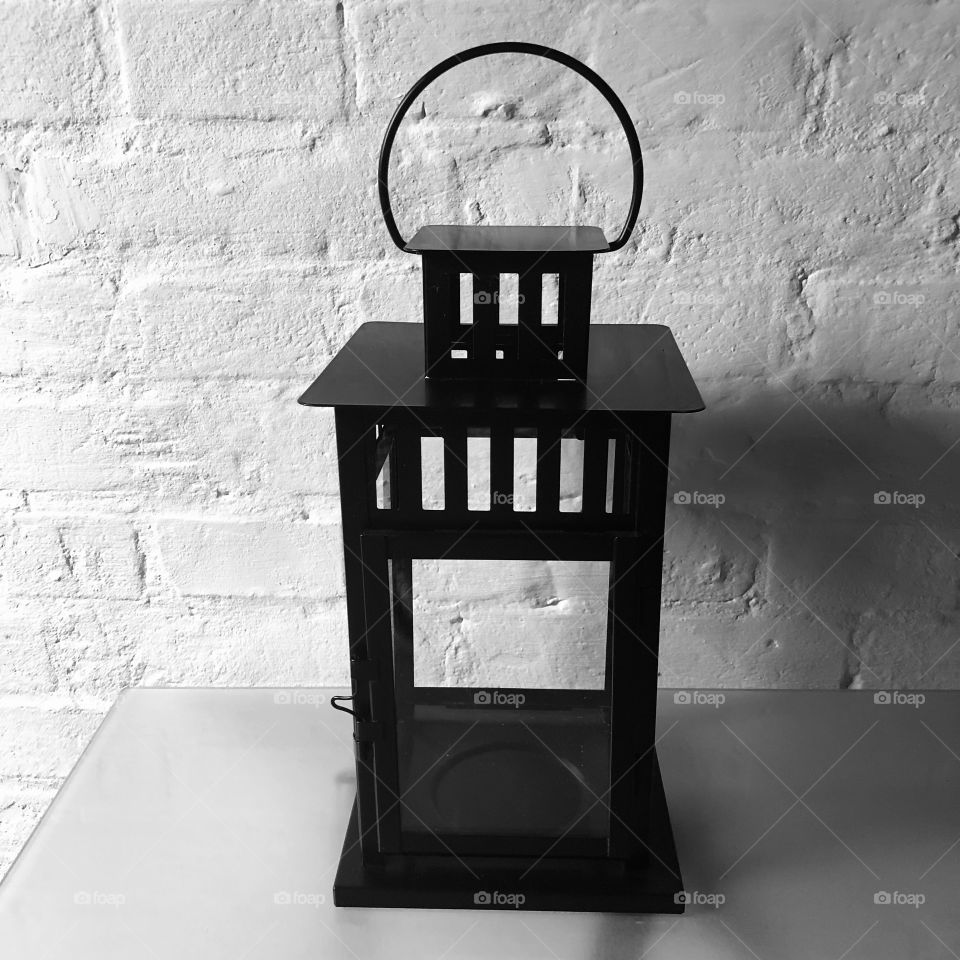 Black lantern lamp on glass table set against white brick wall