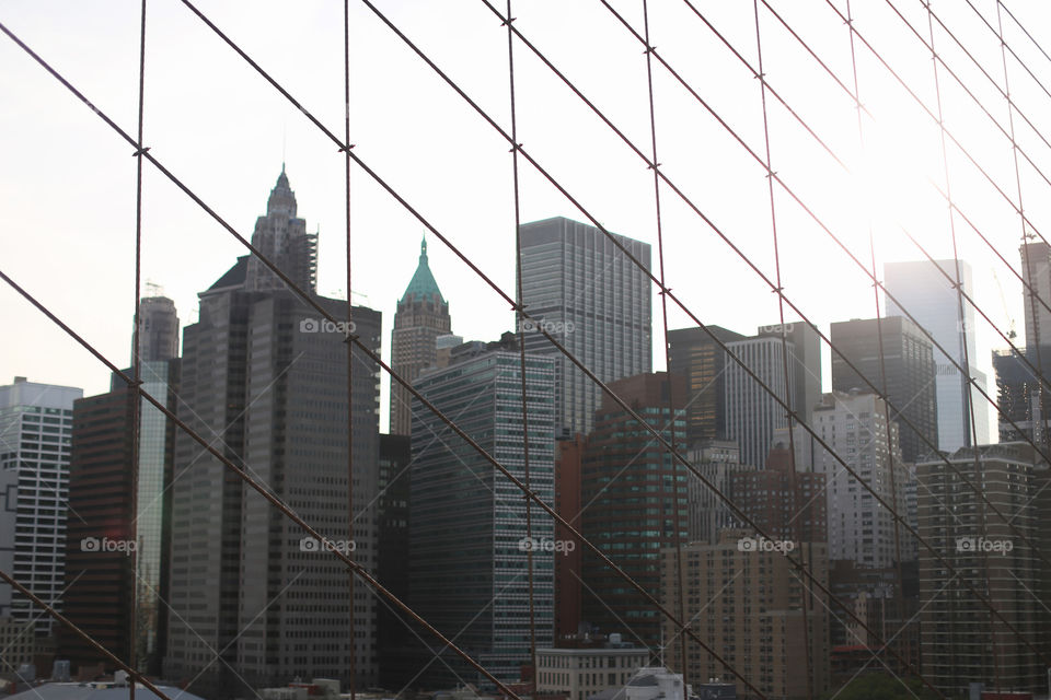 Tall buildings in New York as seen through wires holding a bridge suspended. 
