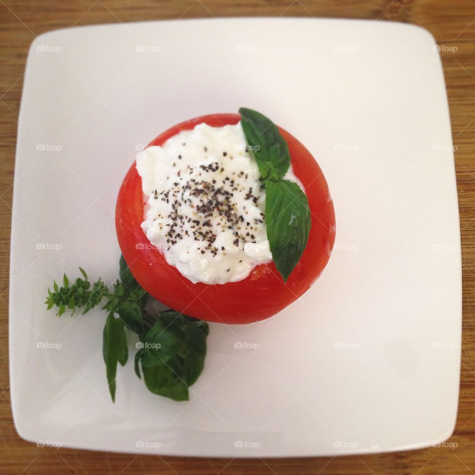 Light Lunch. Tomato stuffed with cottage cheese and basil from my garden on a white plate and wooden cutting board.