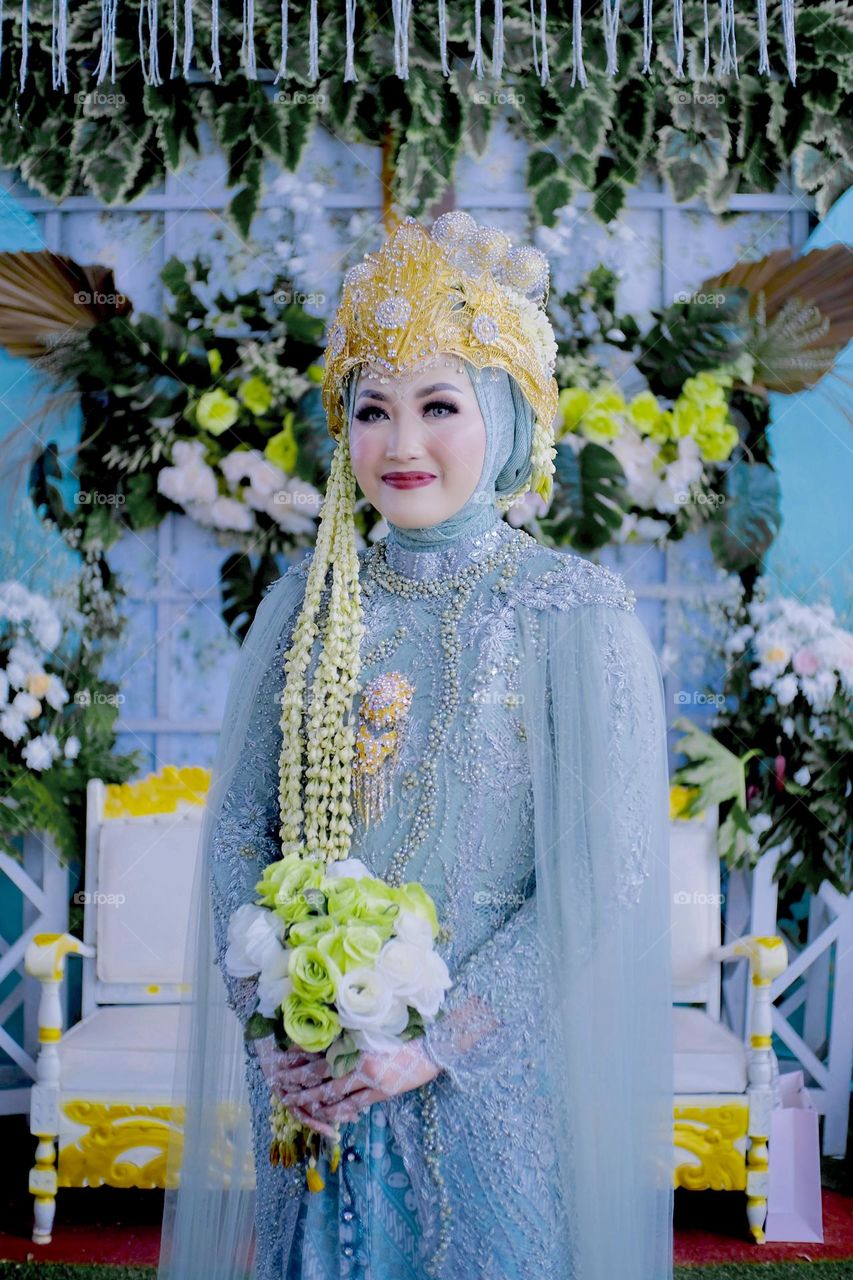 Beautiful asian young woman wearing dress on wedding ceremony, used crown in the head, henna tatto and holding bouquet flower in the hand.