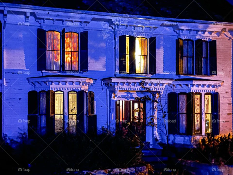 Warm lights of a home shine through the purple glow cast by a nearby building.