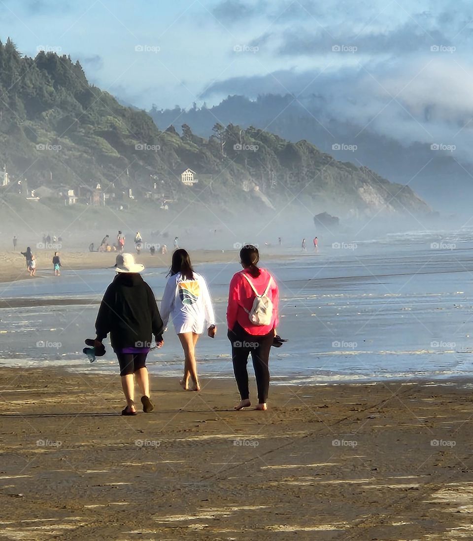 Three people walking down the beach by the Ocean edge on a Summer evening in Oregon