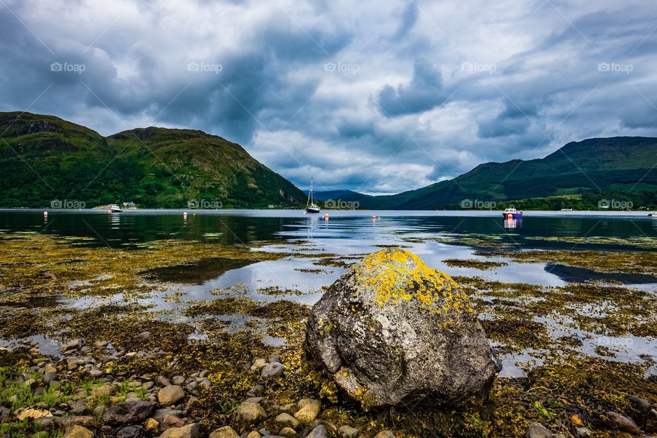 Rock on the Loch. A large rock or Boulder sits on the shore of the Atlantic Ocean sea loch at Airds Bay near Oban, Scotland. 