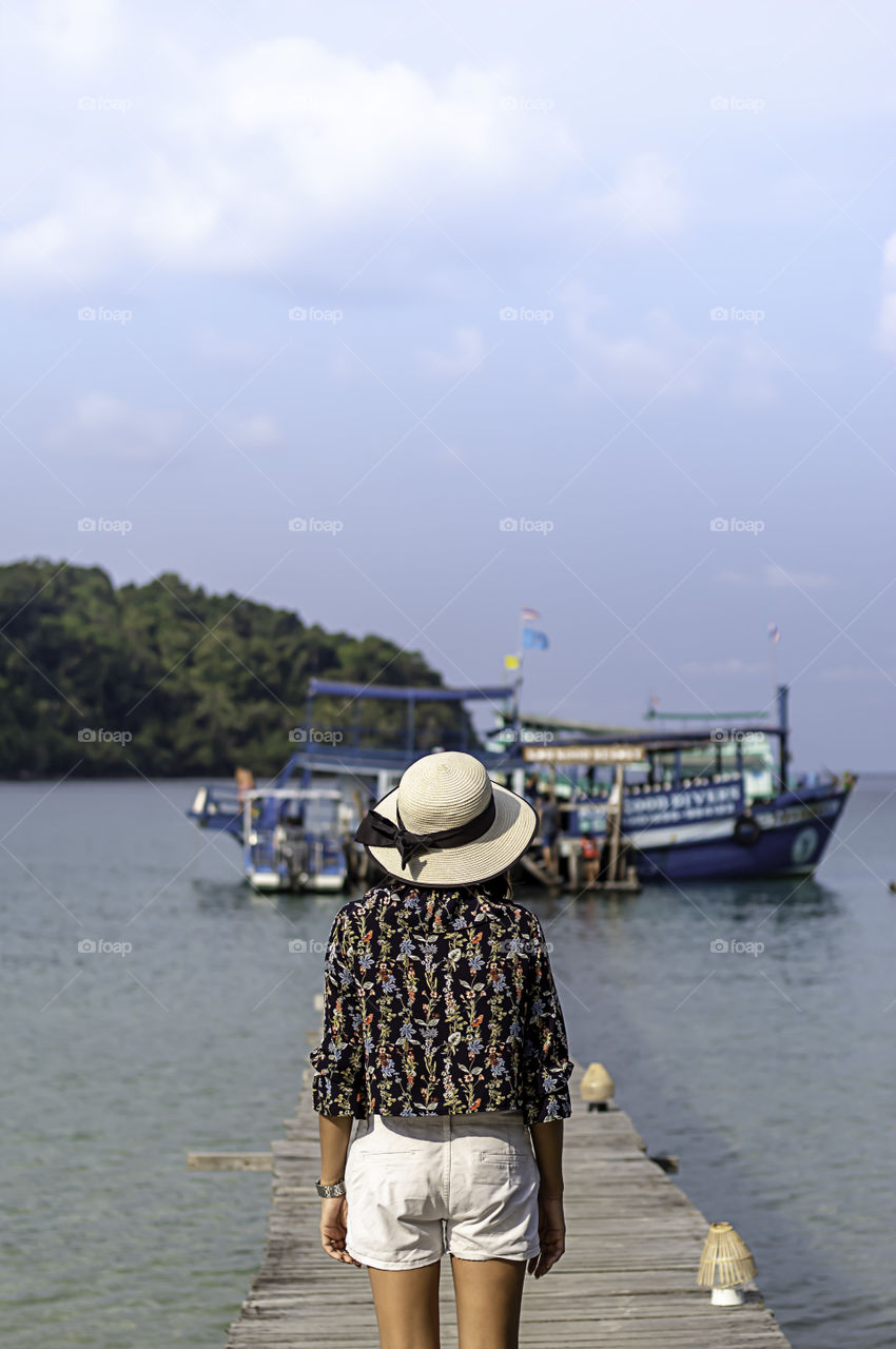 Women Wear a hat on the wooden bridge pier boat in the sea and the bright sky at Koh Kood, Trat in Thailand.