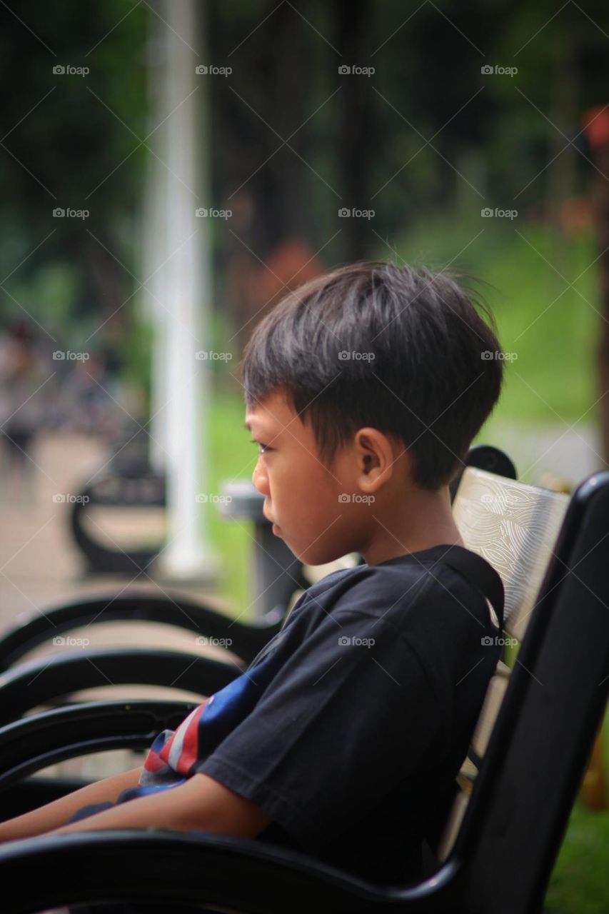 portrait of a boy sitting on a park bench.