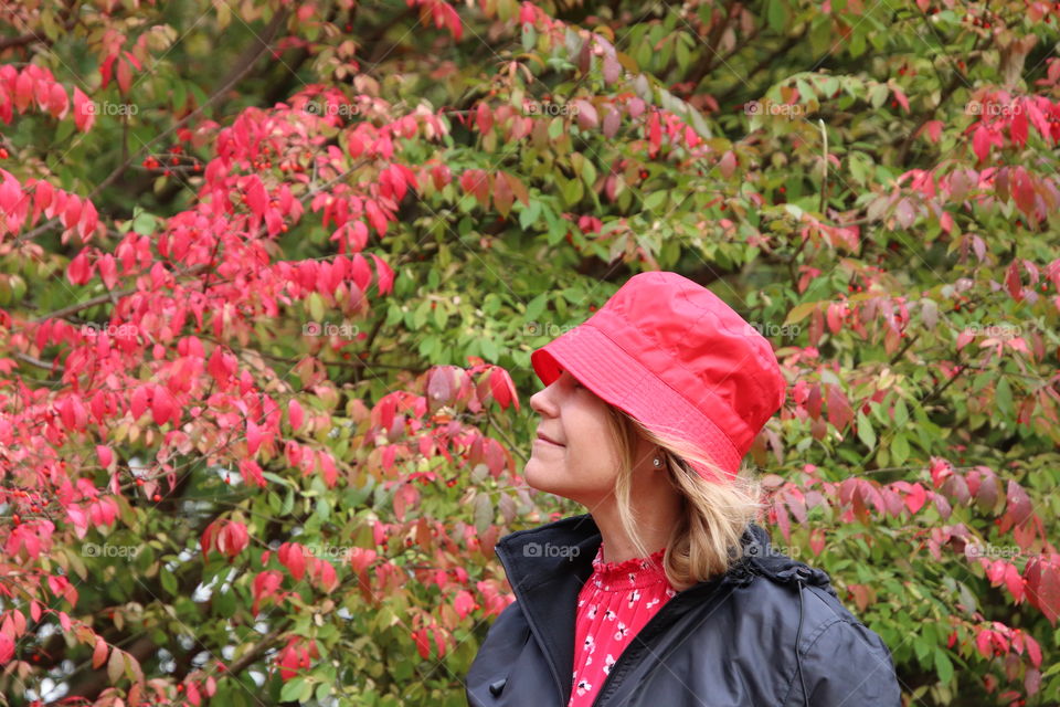 Woman wearing red hat looking at red leaves on biting in bush