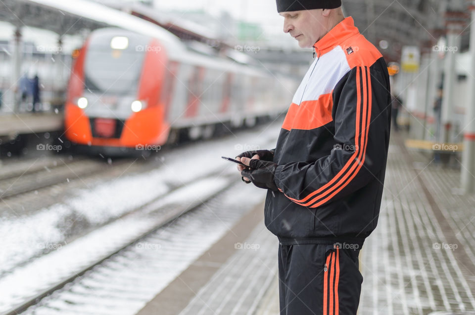 Man using smartphone on the train station in the winter city