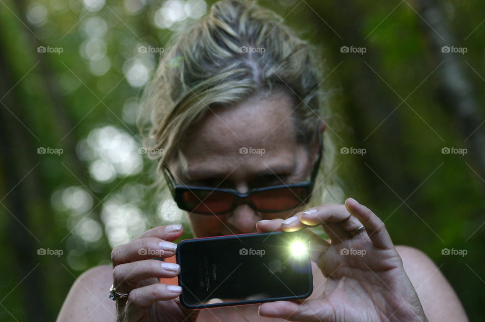 Front view headshot blonde woman taking flash photo with smartphone