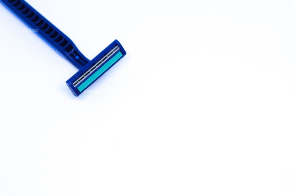 A Blue Razor in The Corner of Minimalist White Background with Flat Lay Shot, Landscape Mode