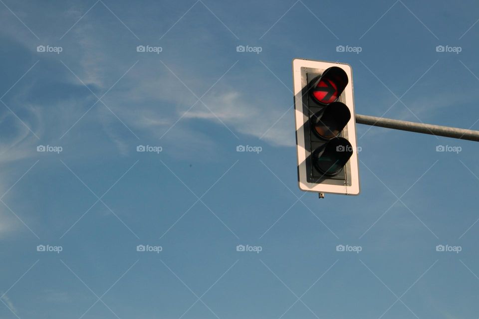 Close-up of a traffic light with a red arrow against a blue sky