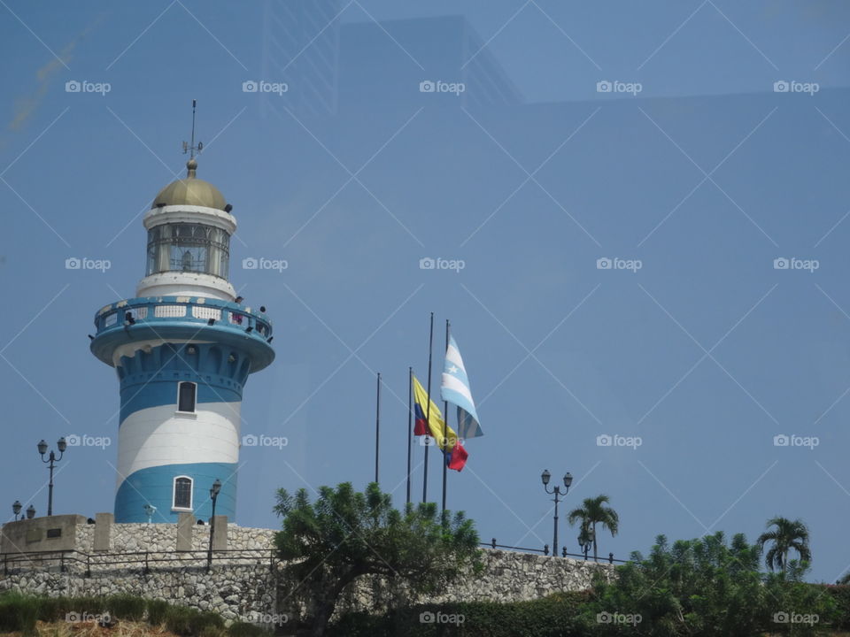 The famous lighthouse on top on Santa Ana Hill in Guayaquil, Ecuador surrounded by a stonewall with flags blowing in the wind on a beautiful day.
