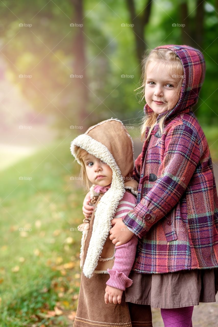 Two little sisters in warm jackets are walking in the park