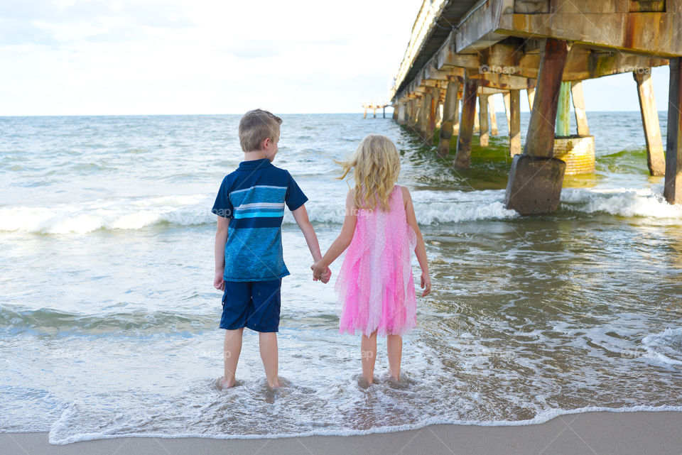 Boy and girl holding hands in the waves at the beach during summer vacation 