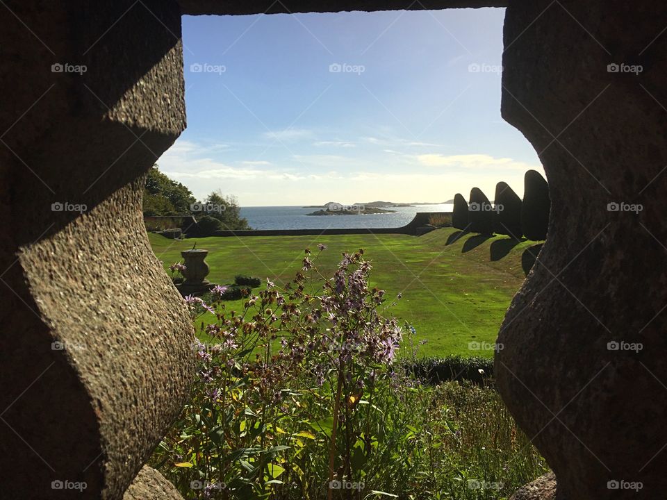 Hole in the stone wall facing the sea and a garden