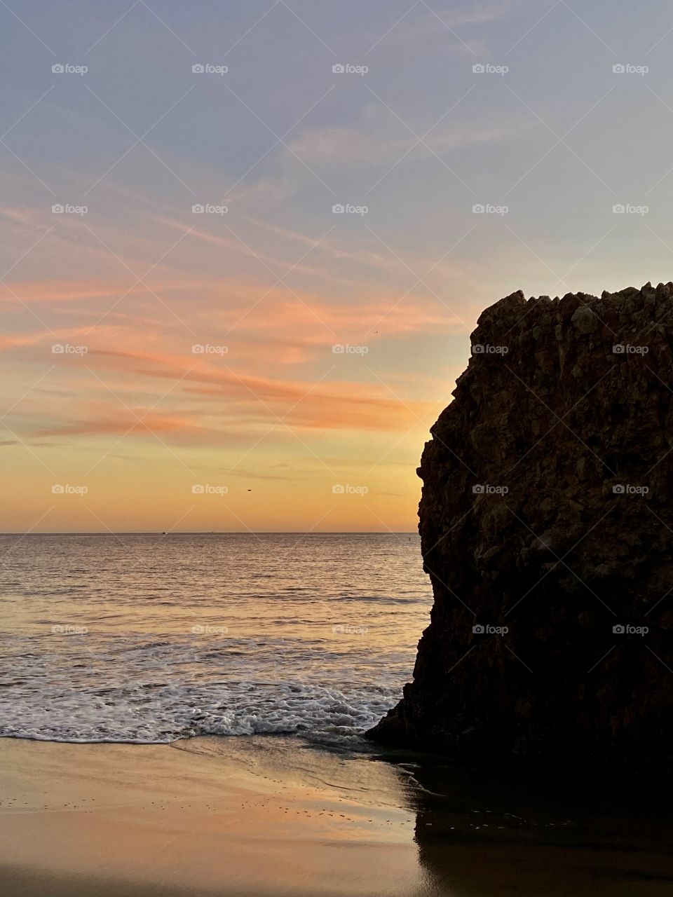 Beautiful sunset on Corona del Mar State Beach with a rock in front of it 