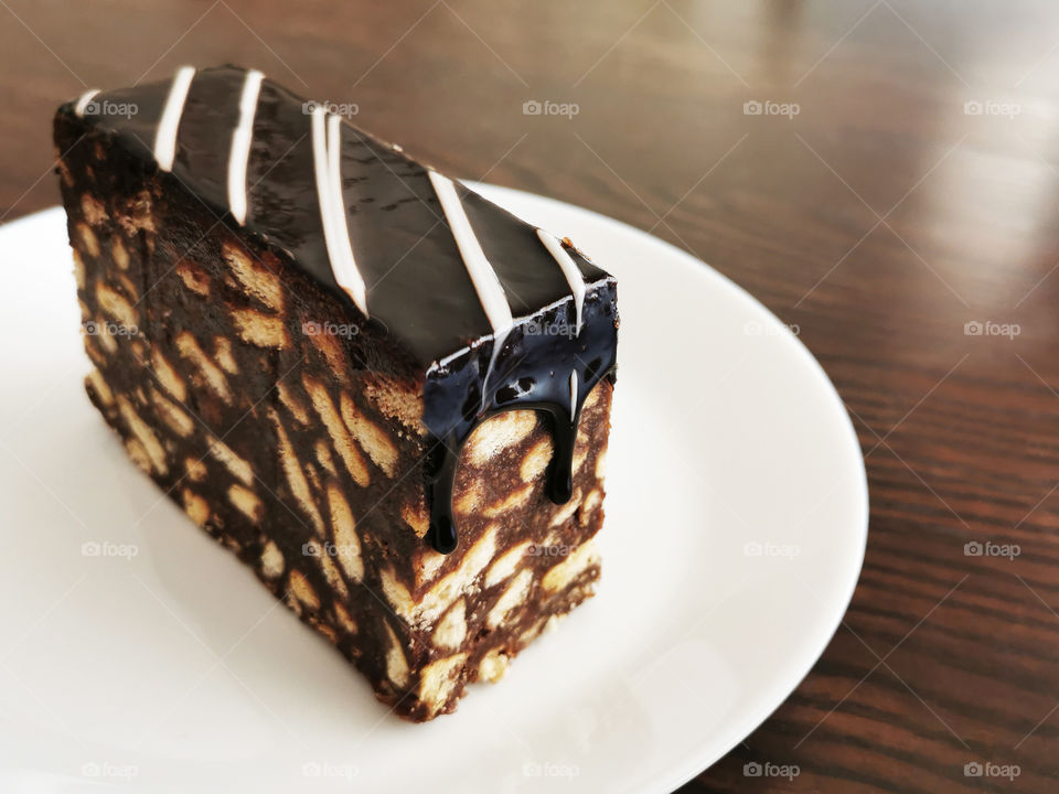 Chocolate cake on a white plate with copy space on the right side. Selective focus at the melted chocolate ganache that falling down on the cake.
