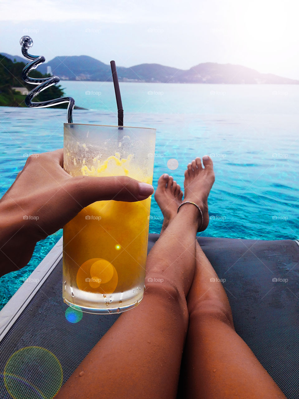 Young woman refreshing with tropical cocktail at the swimming pool 