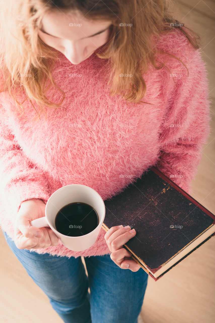 Enjoying the reading a book. Young girl holding book and cup of coffee going to relax with book. View from top