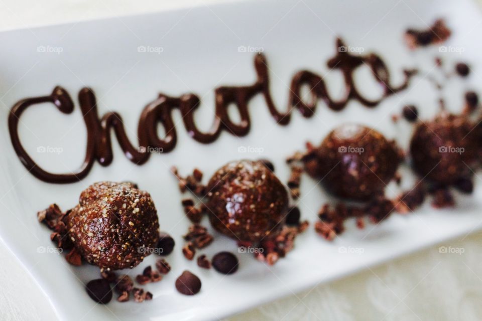 More Chocolate - Nut Butter Cocoa Bites on rectangular white dish with scattered cacao nibs and chocolate chips, and the word "Chocolate" written in chocolate drizzle