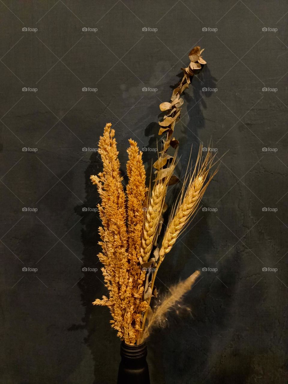 Dried flower bouquet in black glass bottle on wooden table against dull black wall background.Place for text or 
advertisement.View from above