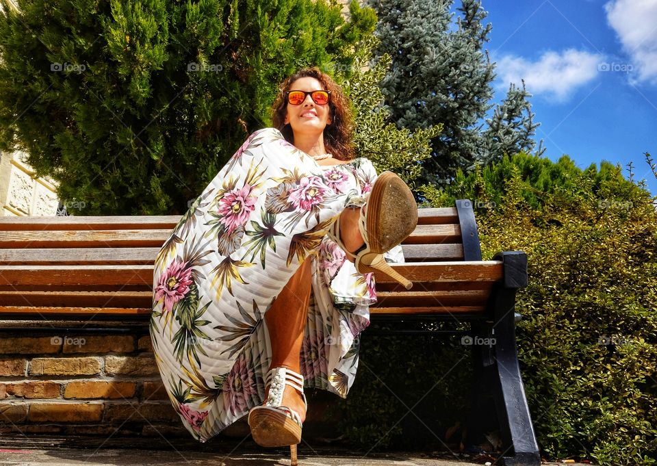 seated woman in floral dress and high heels photographed from below