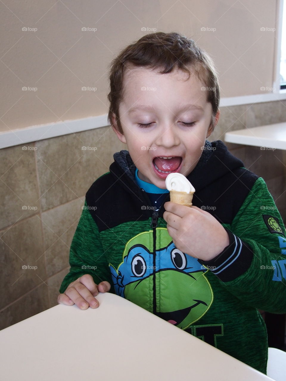 A little boy really enjoys his small vanilla cone that really hits the spot. 