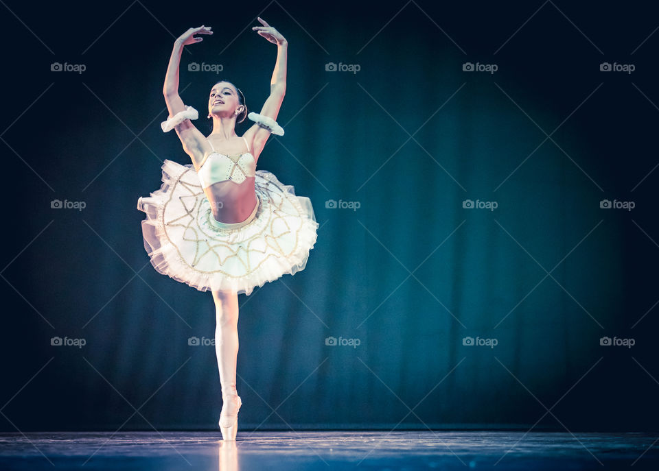 Young Woman Ballerina Dancer Raises Hands Up On Stage In Dark Background
