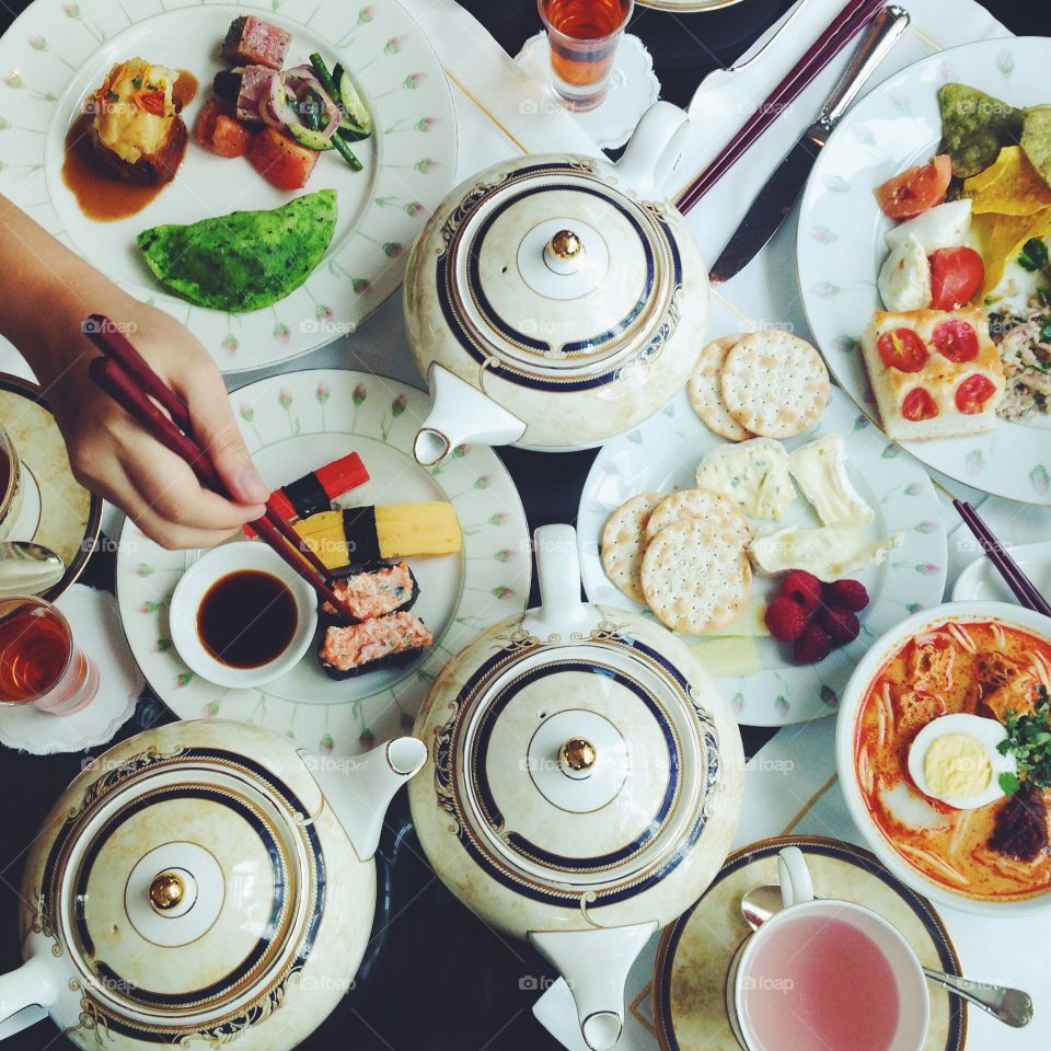 A hand holding chopsticks reaches for sushi on a table filled with food and teapots at the Shangri-La Hotel in Singapore.