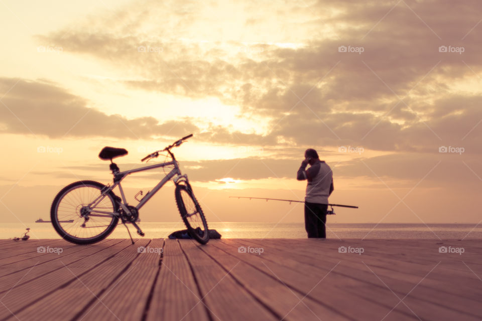 Fisherman Parked His Bicycle And Talking On The Cell Phone At Sunset
