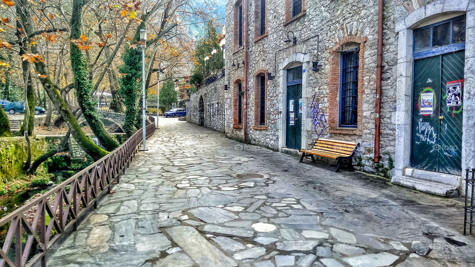 A paved path surrounded by buildings made from stone and trees in Phges Kryas,Livadeia