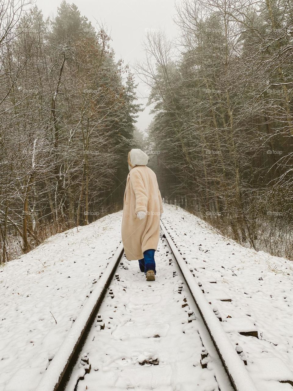 A woman walks alone on a railway in a snowy forest